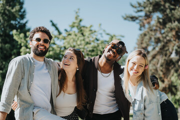 Four friends, two women and two men, smiling and enjoying a sunny day together in a public park, embodying friendship and joy.