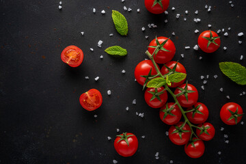 Fresh cherry tomatoes on a black background with spices. Food background. Top view.