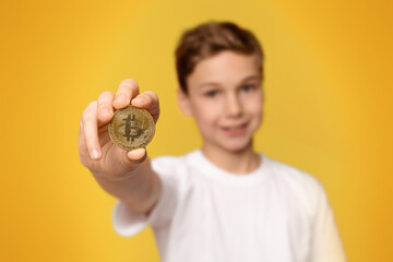 Cryptocurrency and modern finance. Cheerful boy holding golden bitcoin, orange studio background