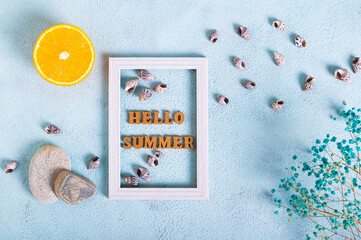 Hello summer text in photo frame, orange, stones, dried flowers and seashells on blue top view