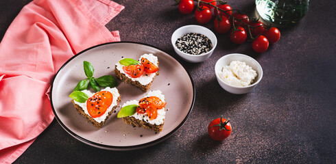 Crostini on rye bread in the shape of a heart with ricotta and tomatoes on a plate web banner
