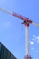 Naklejka premium Red and white crane with heart-shaped hook against blue sky. Romantic crane, love-themed equipment, construction site, Valentine's Day concept.