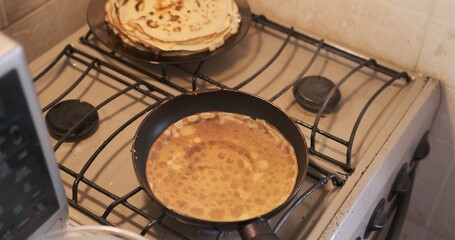A young woman roasts pancakes. Close-up. Turns the pancake over with her fingers on the old biege...