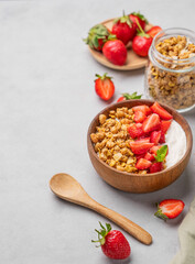 Natural yogurt with granola and strawberries in a wooden bowl on a light background with fresh berries.