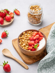 Natural yogurt with granola and strawberries in a wooden bowl on a wooden board on a light background with fresh berries.