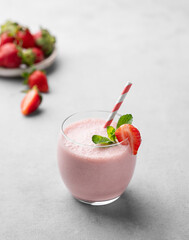 A glass of fresh strawberry smoothie with mint on a light background with fresh berries.