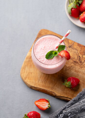 A glass of fresh strawberry smoothie with mint on a wooden board on a blue background with fresh berries.