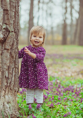 blond baby in a colored dress running in a forest glade with flowers