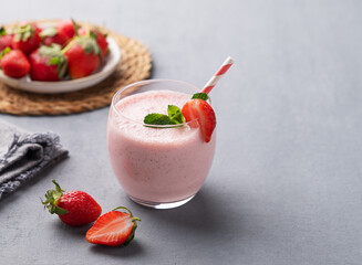 A glass of fresh strawberry smoothie with mint on a blue background with fresh berries and napkin.