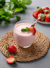 A glass of fresh strawberry smoothie with mint on a blue background with fresh berries.