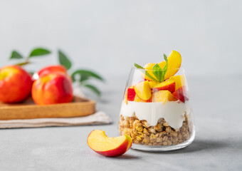 Greek yogurt parfait with peach and granola in a glass on a light background with fresh fruits....