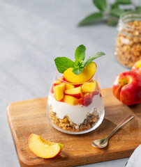 Greek yogurt parfait with peach and granola in a glass on a wooden board on a light background with...