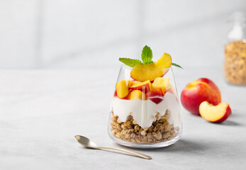 Yogurt parfait with peach and granola in a glass on a light background with fresh fruits. Healthy...