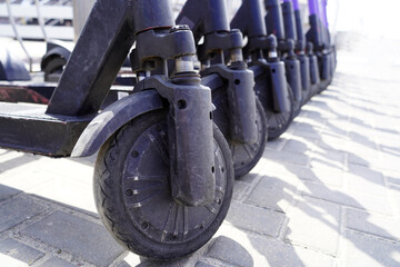 A row of wheels of scooters with scratches on them in the street standing ready for rent