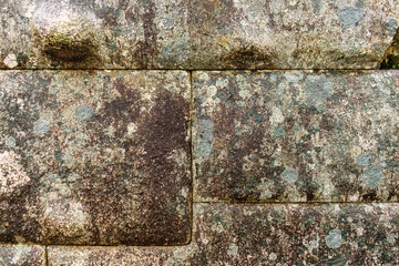 Close-up of ancient stone wall with natural moss and lichen textures, perfect for backgrounds, textures, or archaeological concepts.