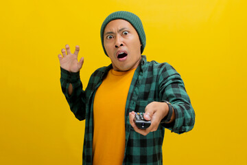 Surprised young Asian man, clad in a beanie hat and casual shirt, watches shocking news on TV while...