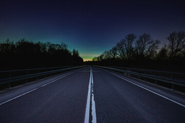 Night asphalt road through the forest, sky with northern lights.