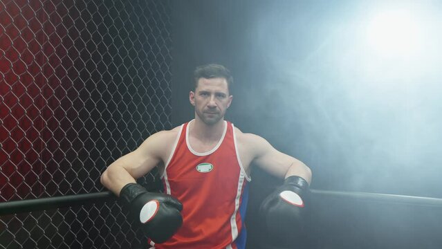 Boxer resting in ring corner. Caucasian male boxer standing in ring corner and looking straight ahead. Fighter resting with arms on ring ropes. Strength and motivation. Sport concept. 4K, UHD