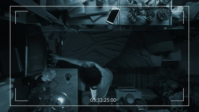 Full top hidden surveillance camera shot of Chinese man or woman walking into cramped flat, turning on TV, laying down on bunk bed, pulling over blanket and watching movie, while relaxing at home