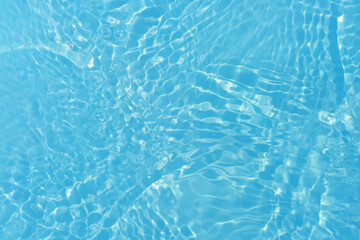 Blue water with ripples on the surface. Defocus blurred transparent blue colored clear calm water surface texture with splashes and bubbles. Water waves with shining pattern texture background.