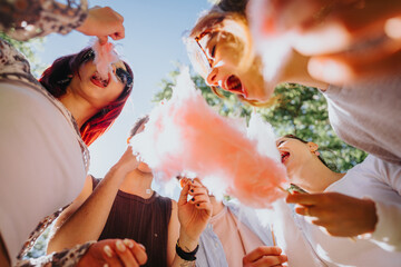 A lively group of friends share moments of joy and laughter while enjoying cotton candy in a sunny park, embodying a true sense of togetherness and fun.