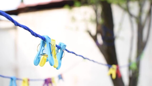 Imagen de un tendedero de ropa color azul en un jard&iacute;n con arboles y ganchos de ropa color azul y amarillo 
