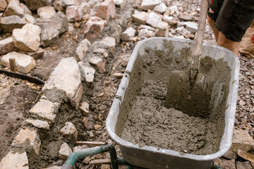 Wheelbarrow with concrete and stones for pathway in cottage garden. Close up of spade with cement,...