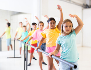 Fototapeta premium Portrait of focused tween girl practicing ballet positions near bar during group class in dance school.