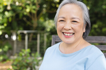 Outdoors, Asian senior female standing, smiling with greenery behind, copy space