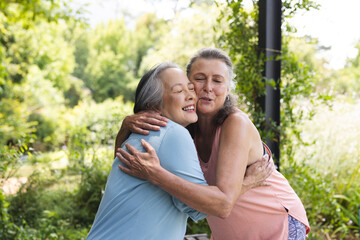 Outdoors, diverse senior female friends hugging, wearing casual clothes