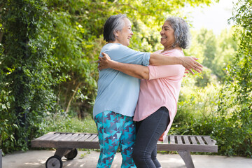 Outdoors, diverse senior female friends embracing warmly