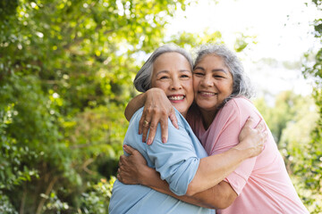Diverse senior female friends hugging outdoors, smiling at camera