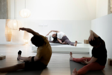 Yoga instructor leads side stretch in a minimalist studio space.