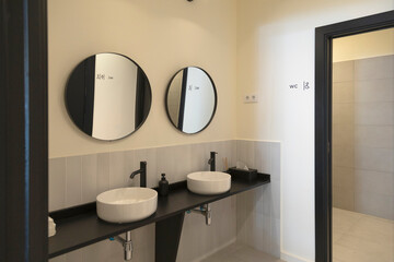 Stylish restroom with twin round mirrors and black fixtures.
