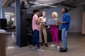 Fototapeta premium In modern office, diverse young team holding devices, discussing work