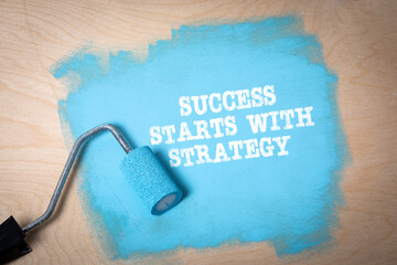 SUCCESS STARTS WITH STRATEGY. Blue paint and paint roller on plywood background