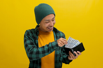 Excited Asian man, dressed in a beanie hat and casual shirt, smiles at the camera while proudly displaying a wallet filled with money, representing finance, investment, and money saving concepts
