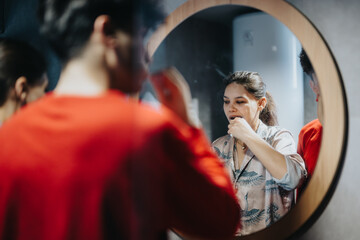 A daily routine captured with a young woman brushing her teeth while reflected in a round bathroom...