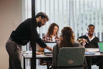 A diverse group of young business professionals collaborates on project analysis, discussing growth trends and statistics around a laptop in a well-lit office environment.