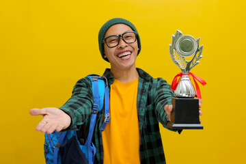 Happy young Asian student, adorned in a beanie hat, eyeglasses, and a casual shirt, proudly lifts...