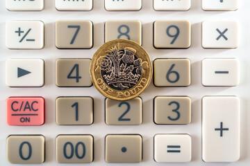 British one pound coin placed on top of the calculator buttons. Concept for business and finance.