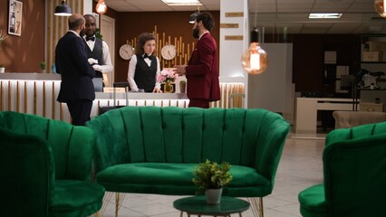 Businessmen start check in formalities, exchanging information with hotel staff members at front...