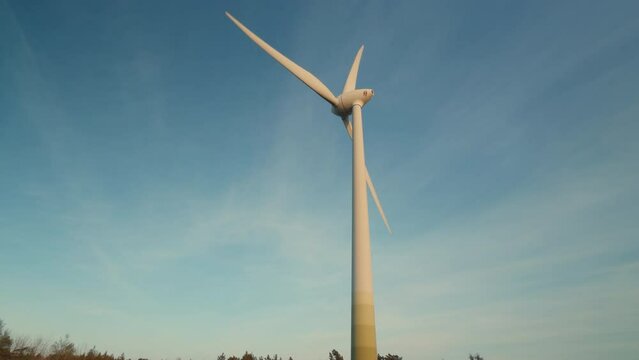A wind turbine is tall and white, standing in a field. The sky is blue and clear, with no clouds in sight. Concept of calm and serenity, as the wind turbine stands tall