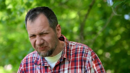 A white European man sneezes and blows his nose into a paper napkin against a green background. Spring exacerbation of allergy to poplar fluff. Allergy in adults hay fever