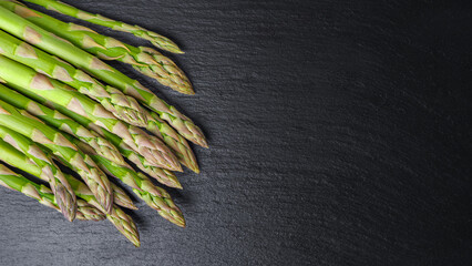 Bunch of fresh green asparagus on black slate background. Edible sprouts, stems of sparrowgrass. Healthy food, fresh vegetable, ingredient for cooking Top view, banneer, header with copy space