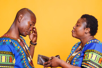 Angry wife showing empty wallet with no money to upset frustrated husband. African american man and...