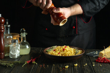 Adding ground pepper to a plate of food by the cook hands for aroma and taste. Delicious pasta on the kitchen table in a plate.