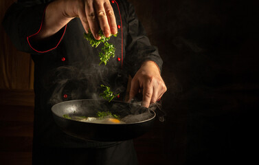 Adding green parsley to a hot frying pan in the hand of a chef in a restaurant kitchen.