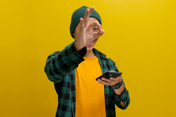 A young Asian man, dressed in a beanie hat and casual clothes, makes an OK sign gesture while...