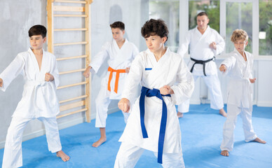 Concentrated teenager in white kimono practicing punches in gym during group martial arts workout. Shadow fight, combat sports training concept ..